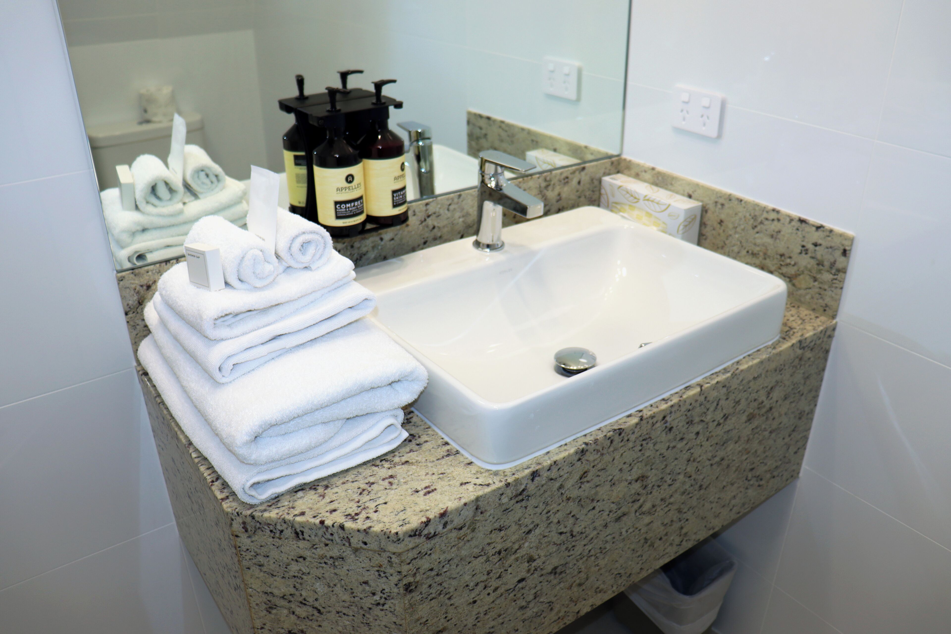 Casa de banho com bancada de granito, lavatório branco e toalhas cuidadosamente dobradas.