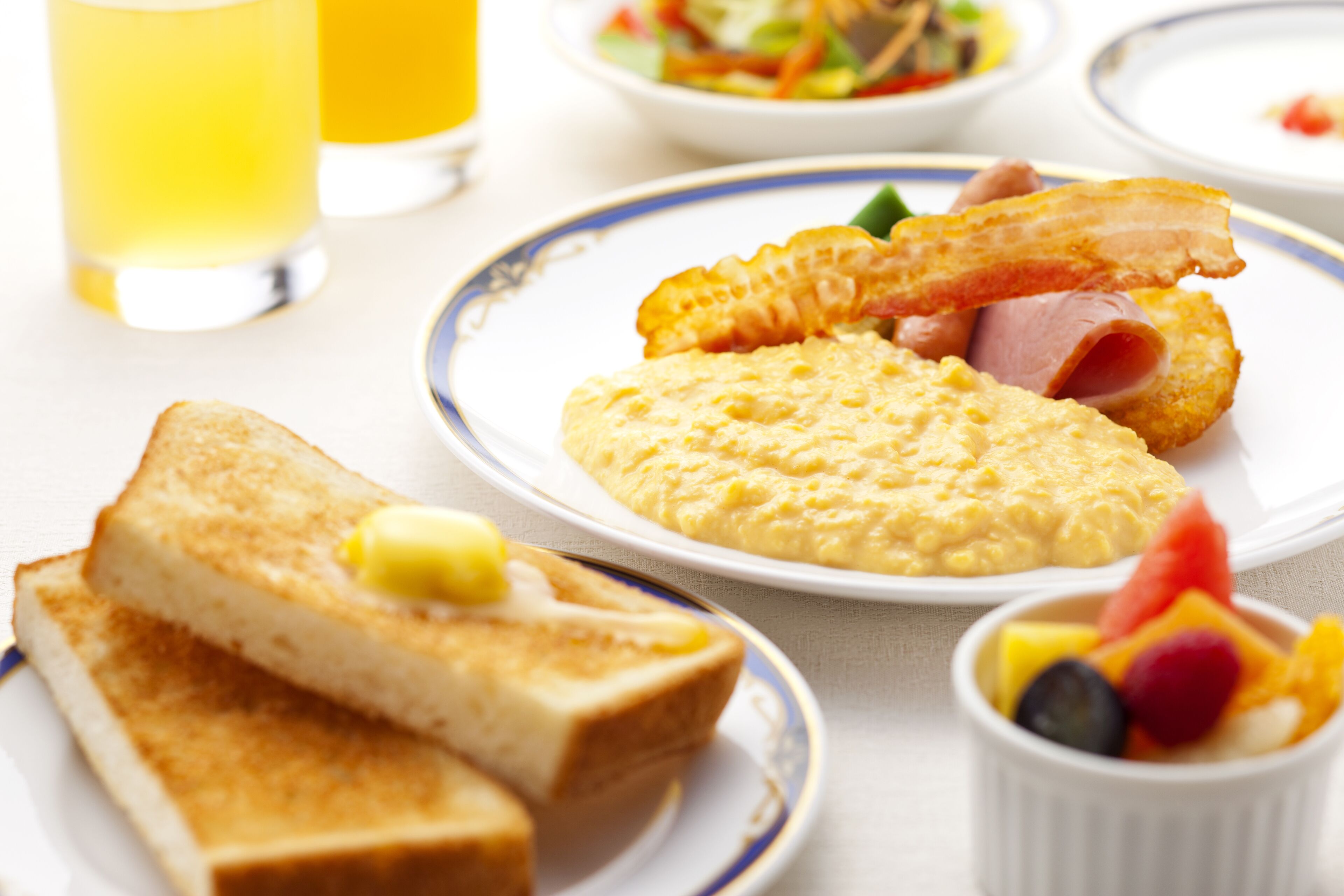 Une assiette de petit-déjeuner comprenant des toasts, des œufs brouillés, du bacon et une salade de fruits.