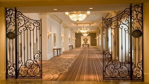 Un pasillo de hotel con puertas de metal ornamentadas, alfombra estampada y un candelabro.