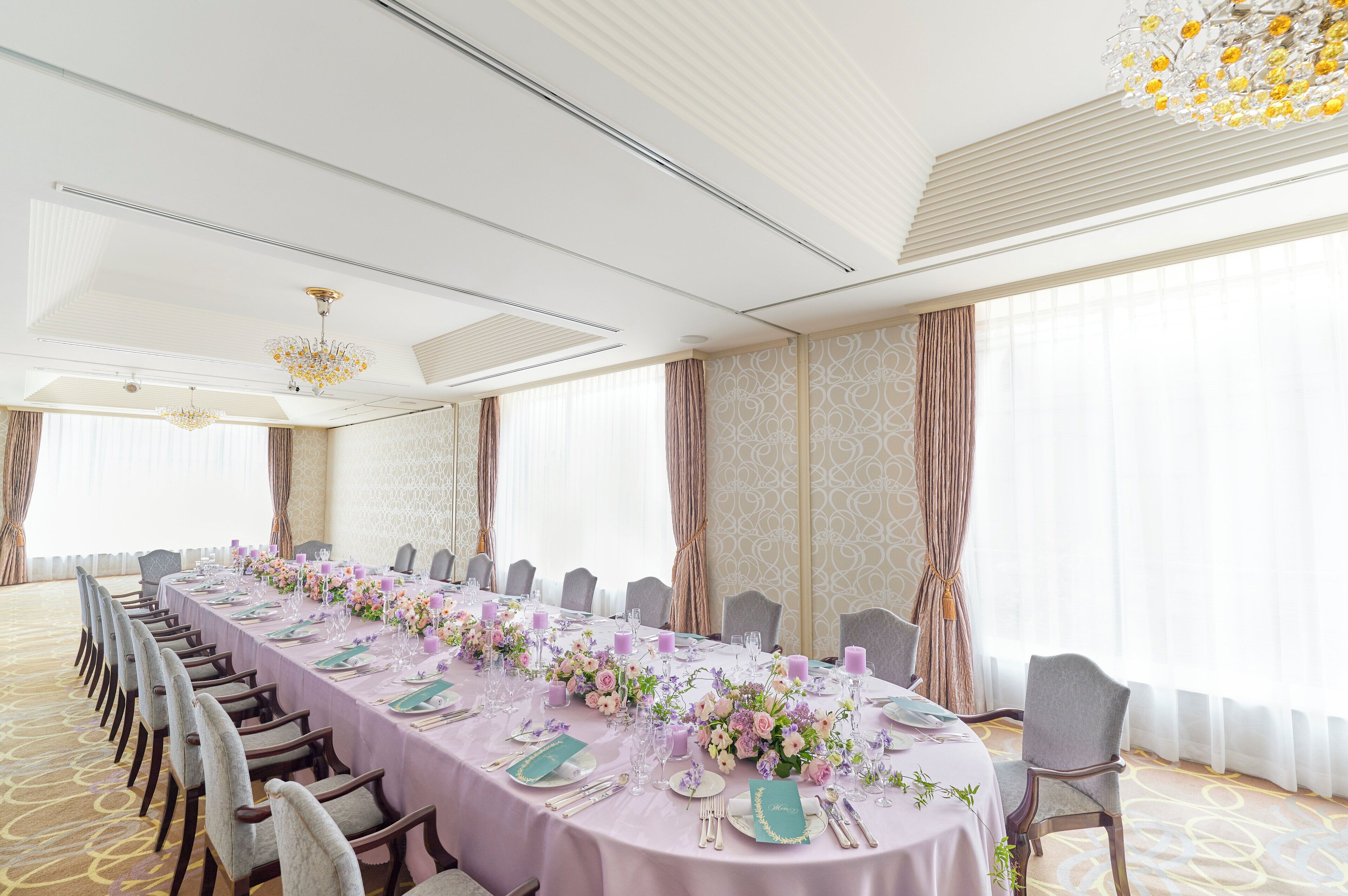 A conference room with a long table set for a meeting, equipped with chairs and floral centerpieces.