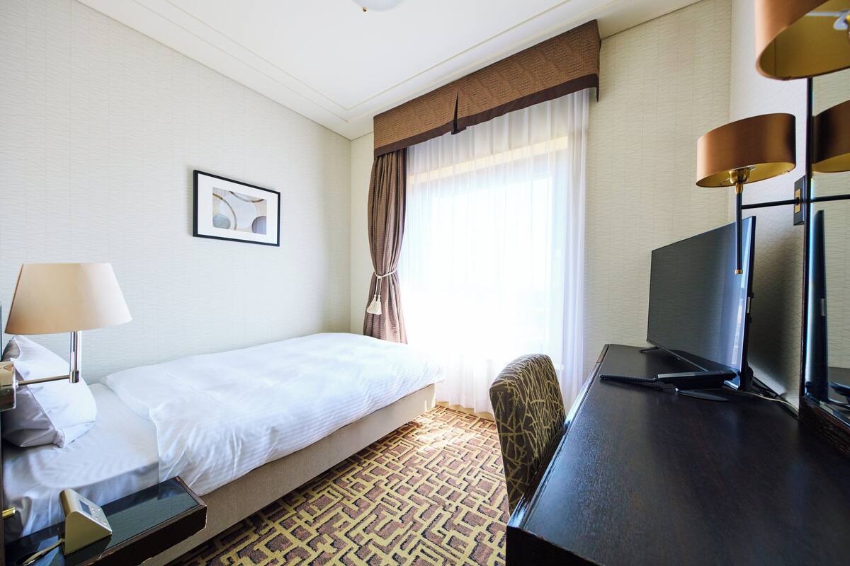 Een hotelkamer met een bed, een bureau met televisie, een lamp en een stoel.
