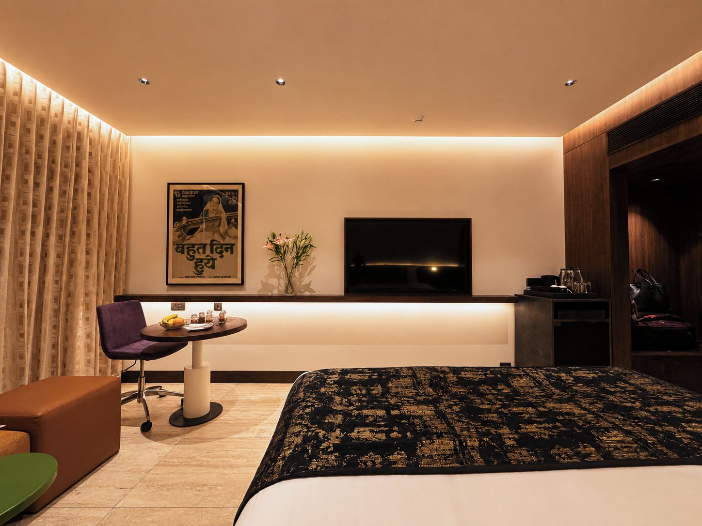 A modern hotel room with a bed, a desk, a chair, a TV, and a poster on the wall.