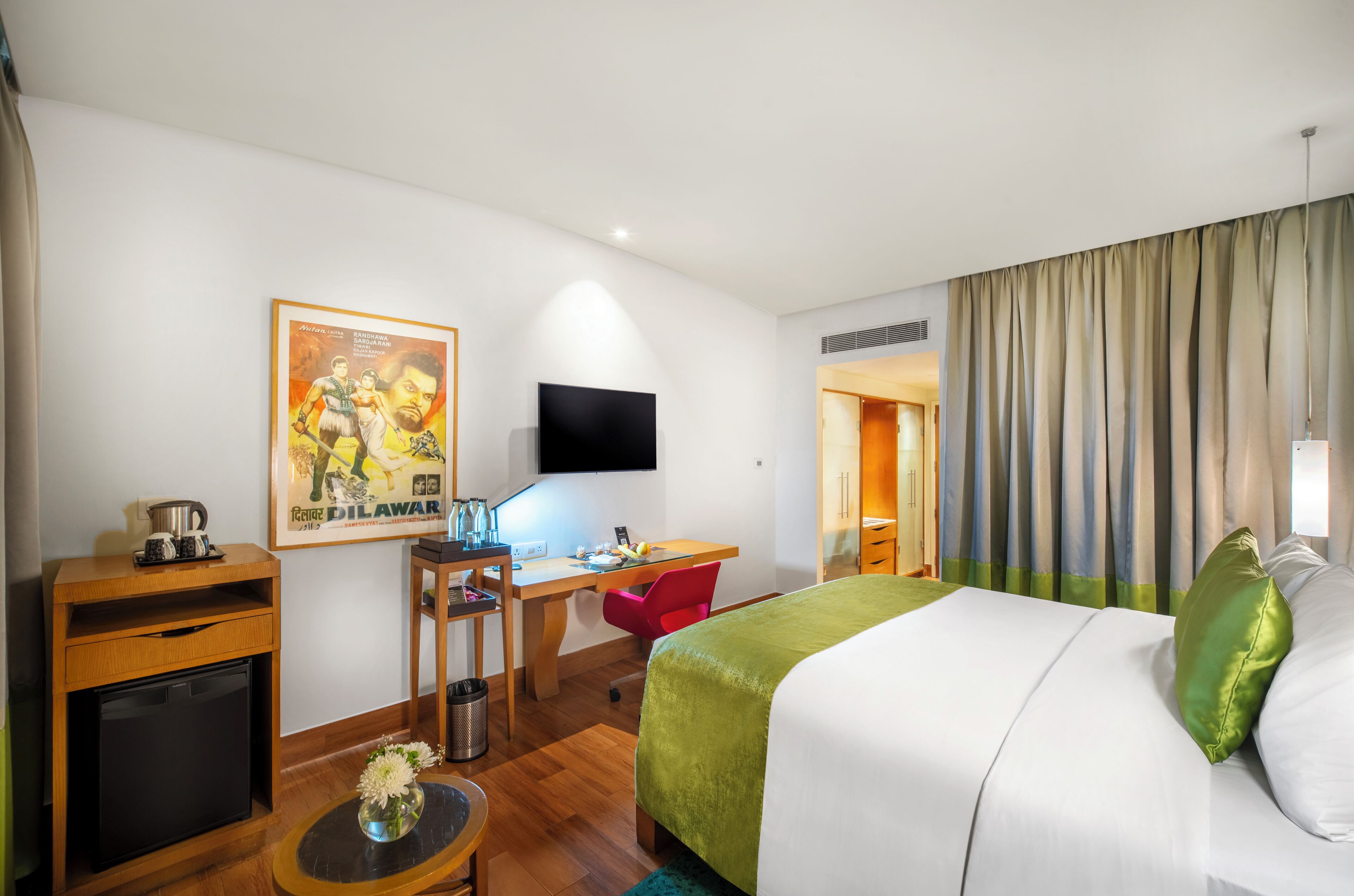 A hotel room with a bed, desk, chair, television, and a small kitchenette.