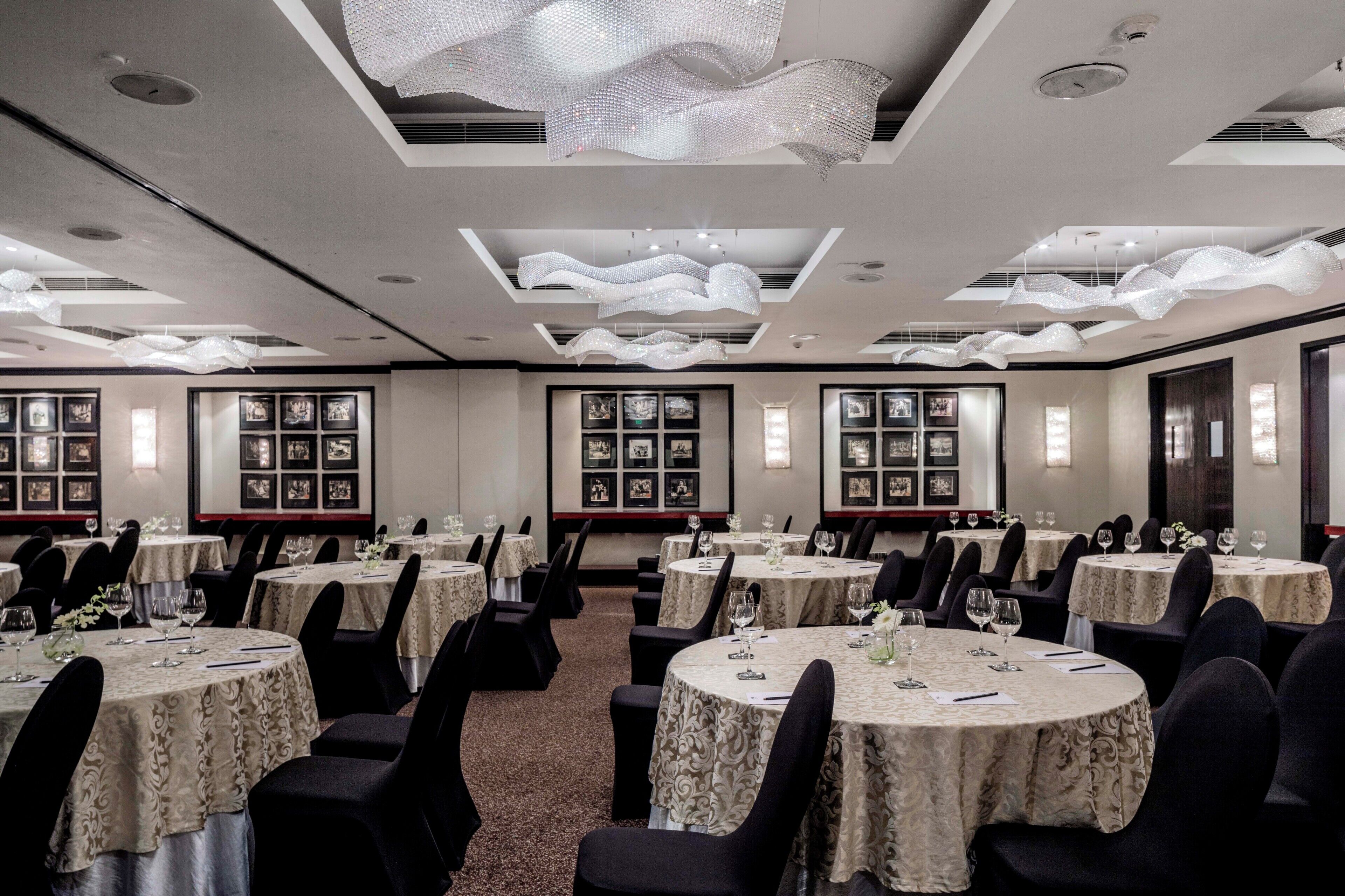 A banquet hall with round tables, black chairs, and framed pictures on the walls.