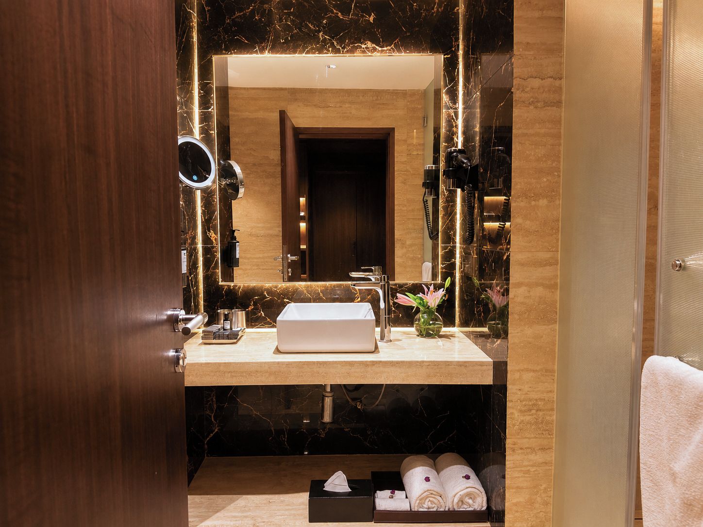 A modern bathroom with a marble vanity, a large mirror, and a towel rack.