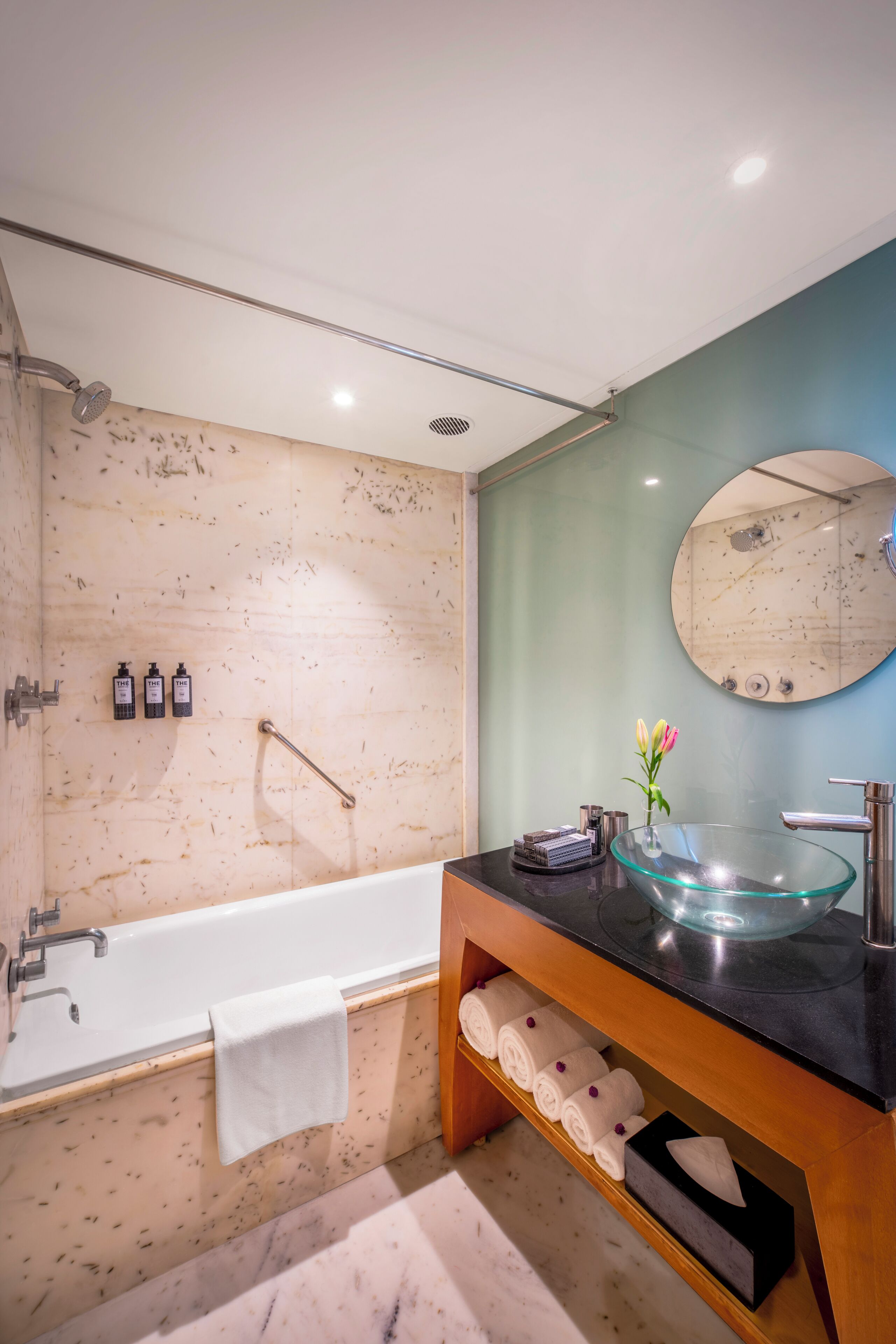 Un baño moderno con una bañera acristalada, un espejo redondo y un mueble de tocador de madera con encimera negra.