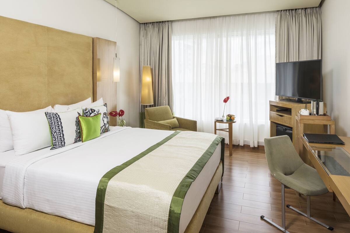 Une chambre d’hôtel avec un grand lit, un bureau avec un ordinateur, une télévision et une chaise.