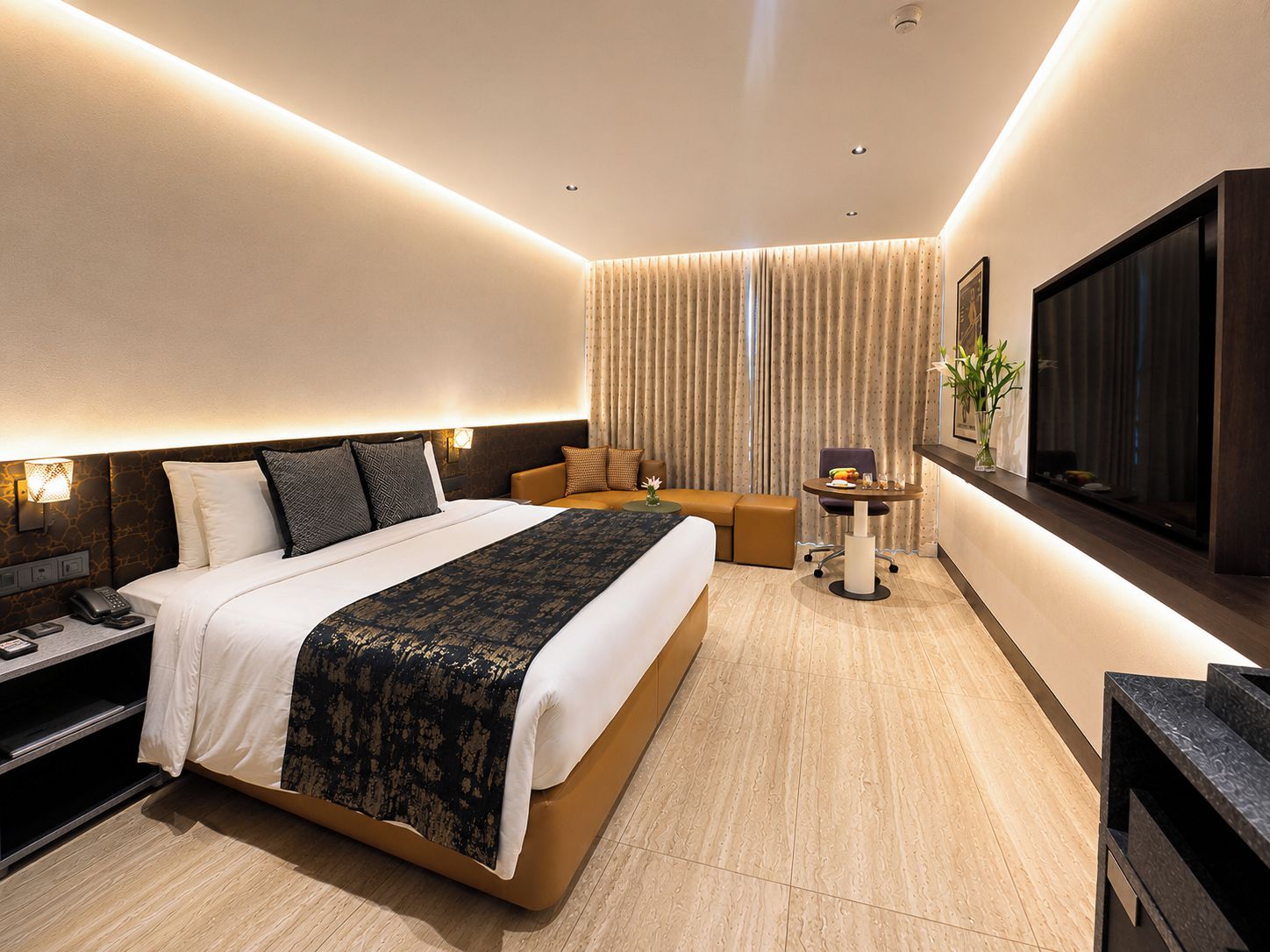 A modern hotel room with a large bed, a sofa, a small table, and a TV.