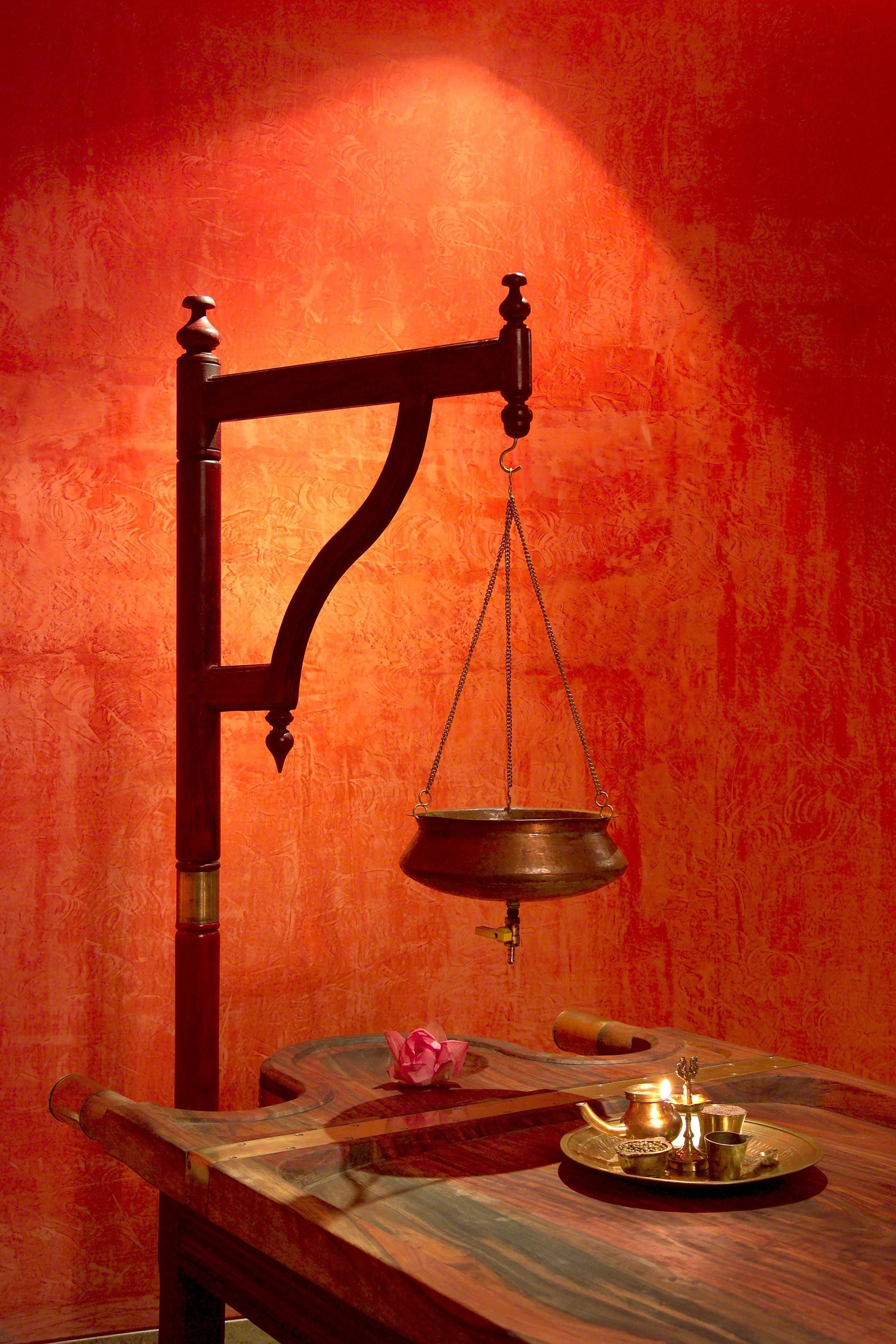 Uma balança tradicional com uma tigela de latão suspensa em uma estrutura de madeira, um banco de madeira, e uma mesa com um tabuleiro de latão e uma flor rosa.