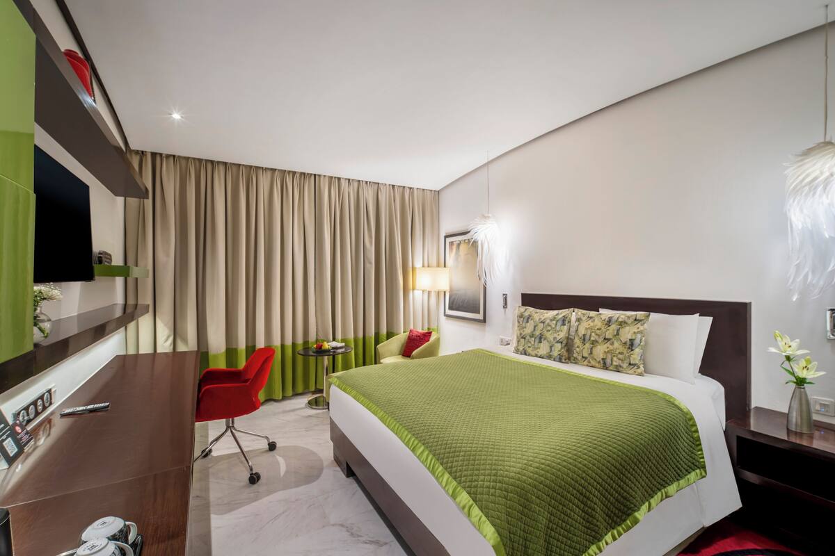 Une chambre d’hôtel avec un lit, un bureau, une chaise, une lampe et un téléviseur.