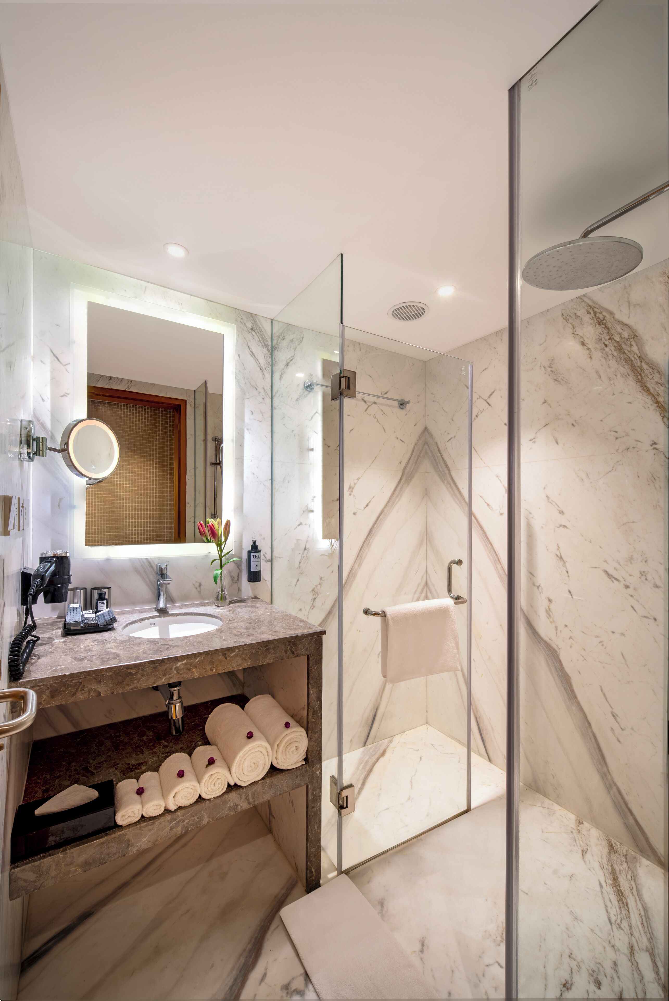 A modern bathroom with a glass-enclosed shower, a marble sink, and a vanity with towels.