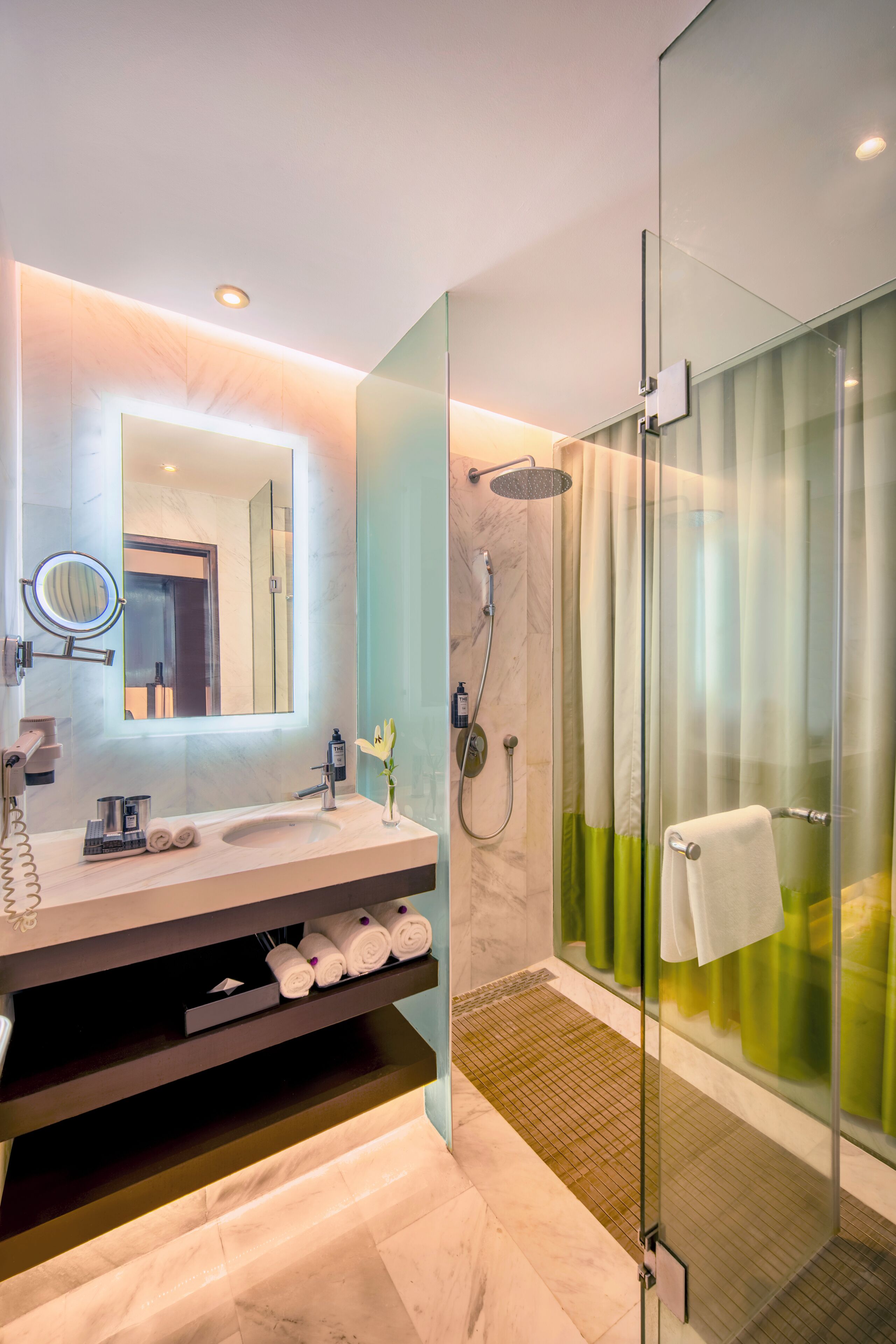 A modern bathroom with a glass shower enclosure, a marble sink, and a vanity with toiletries.