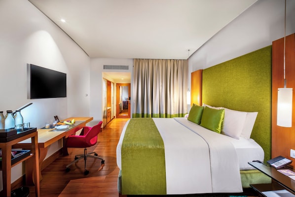 Habitación de hotel con cama, escritorio, silla y televisor montado en la pared.