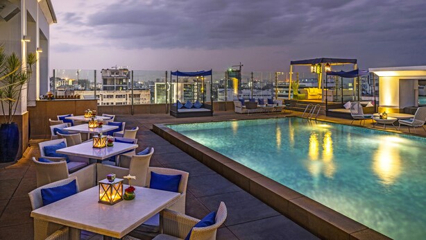 A rooftop pool area with tables and chairs, a clear view of the city skyline, and a covered seating area. - The Park Chennai (Chennai)