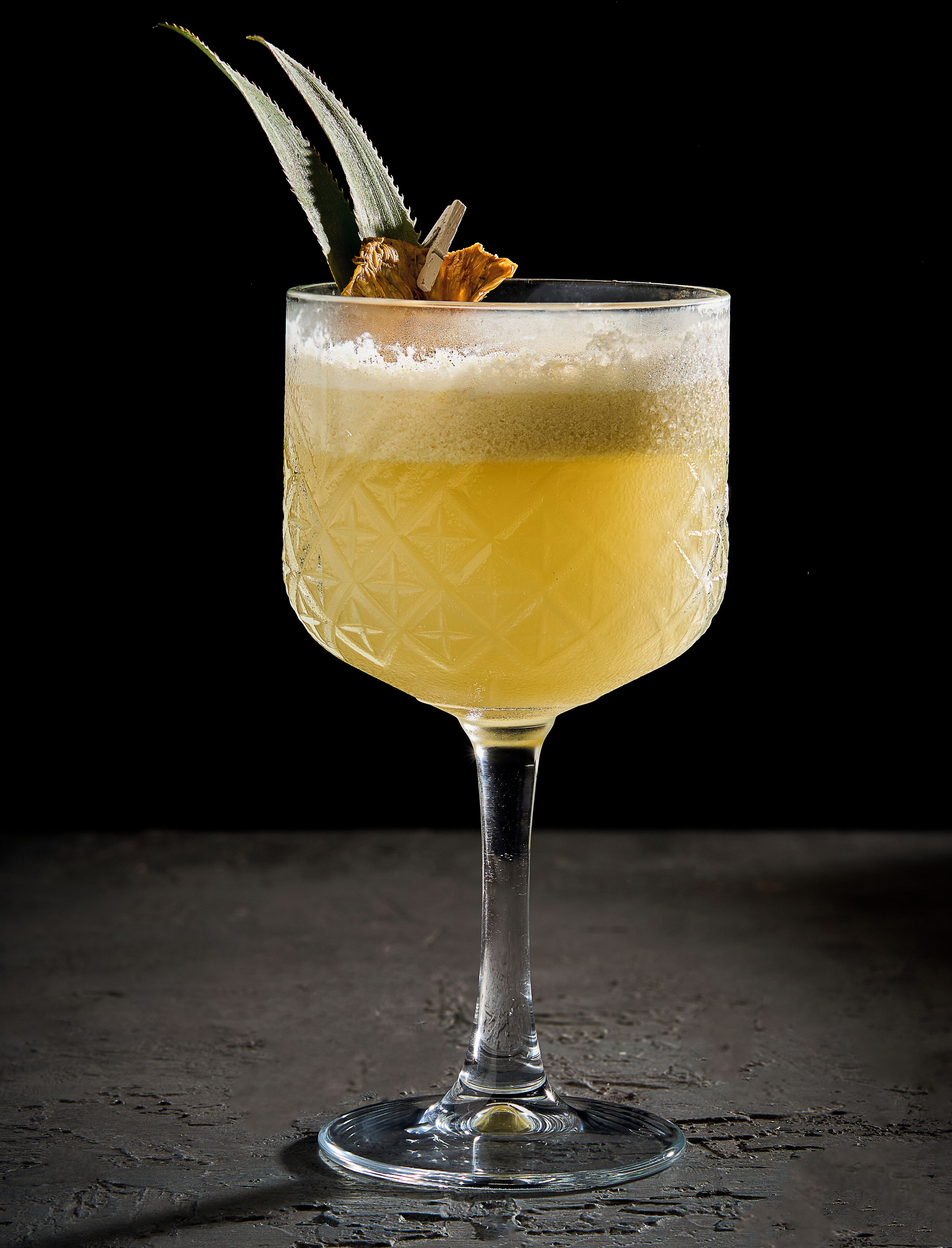 Un verre à cocktail contenant un liquide transparent, un élément de décoration et un motif texturé sur le verre.