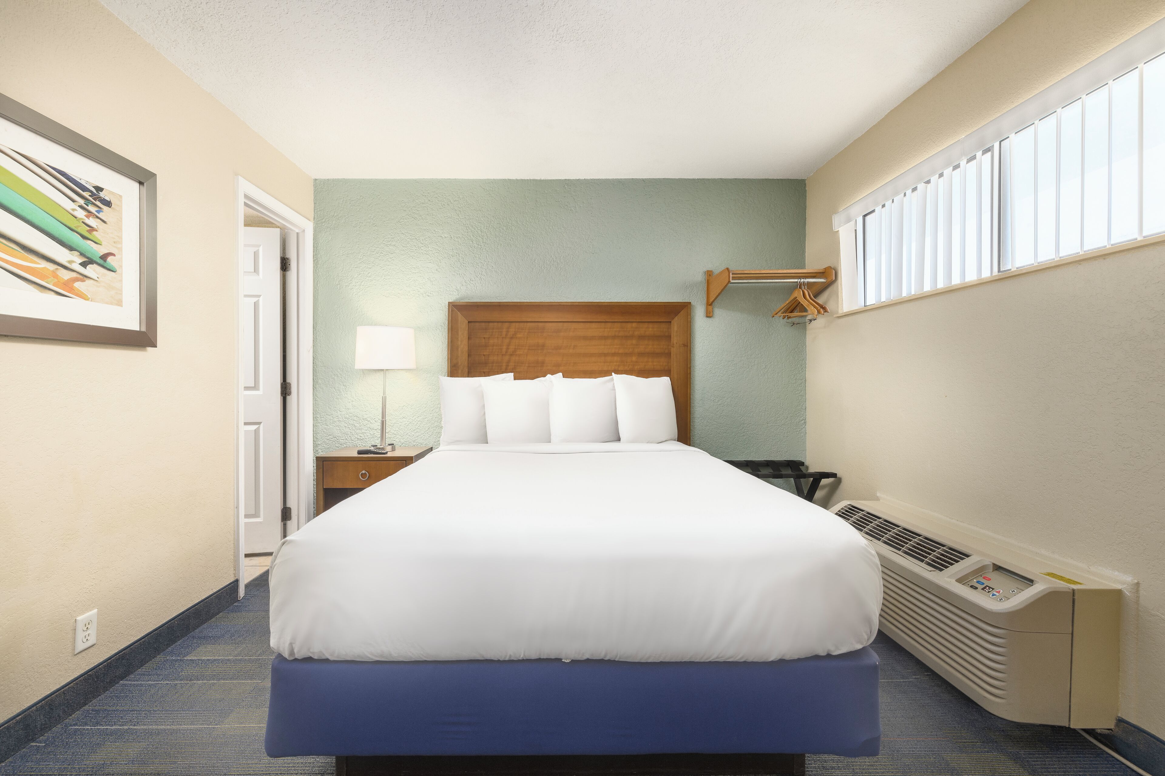 Habitación de hotel con cama, mesita de noche, lámpara, ventana con persianas y calefactor en la pared.