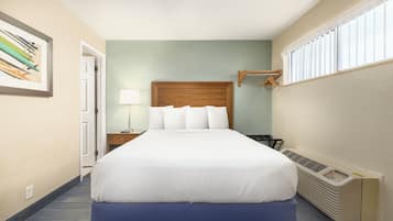 Habitación de hotel con cama, mesita de noche, lámpara, ventana con persianas y calefactor en la pared.