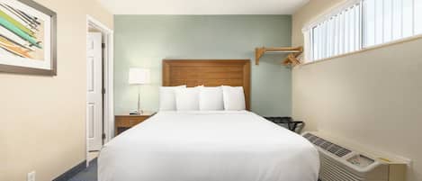 Habitación de hotel con cama, mesita de noche, lámpara, ventana con persianas y calefactor en la pared.
