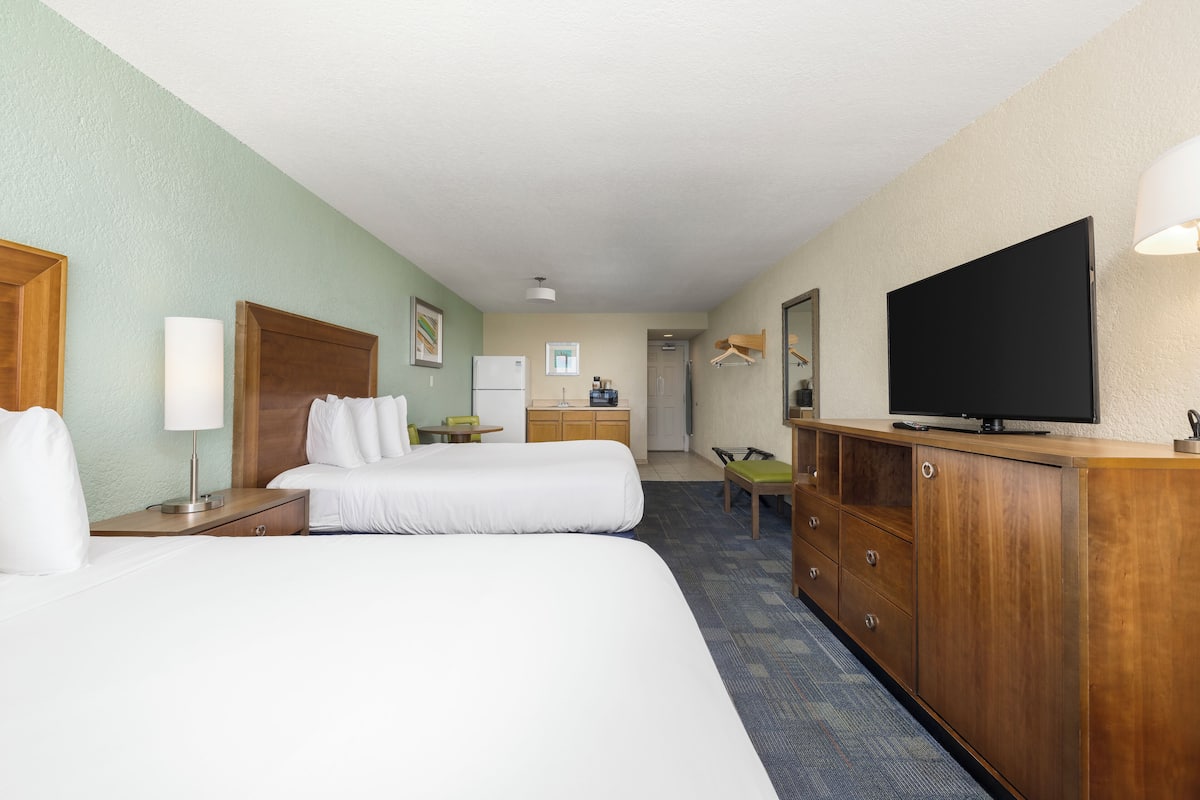 A hotel room with two beds, a desk, a TV, and a bathroom visible in the background.