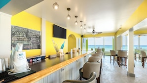 A bar area with a chalkboard menu, bar stools, and a view of the ocean.