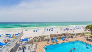 A beachside pool area with lounge chairs and umbrellas, a swimming pool, and a view of the ocean.