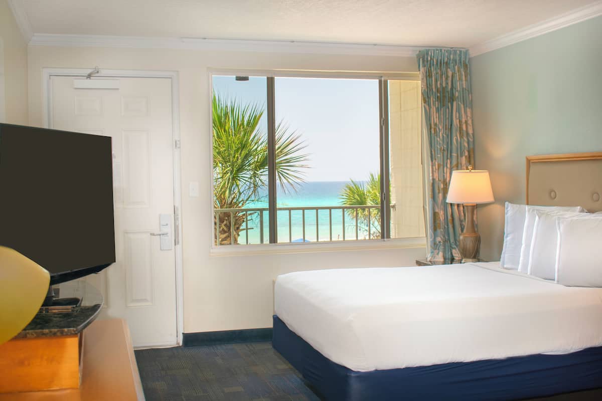 A hotel room with a bed, a TV, a window with a view of the ocean, and a lamp.