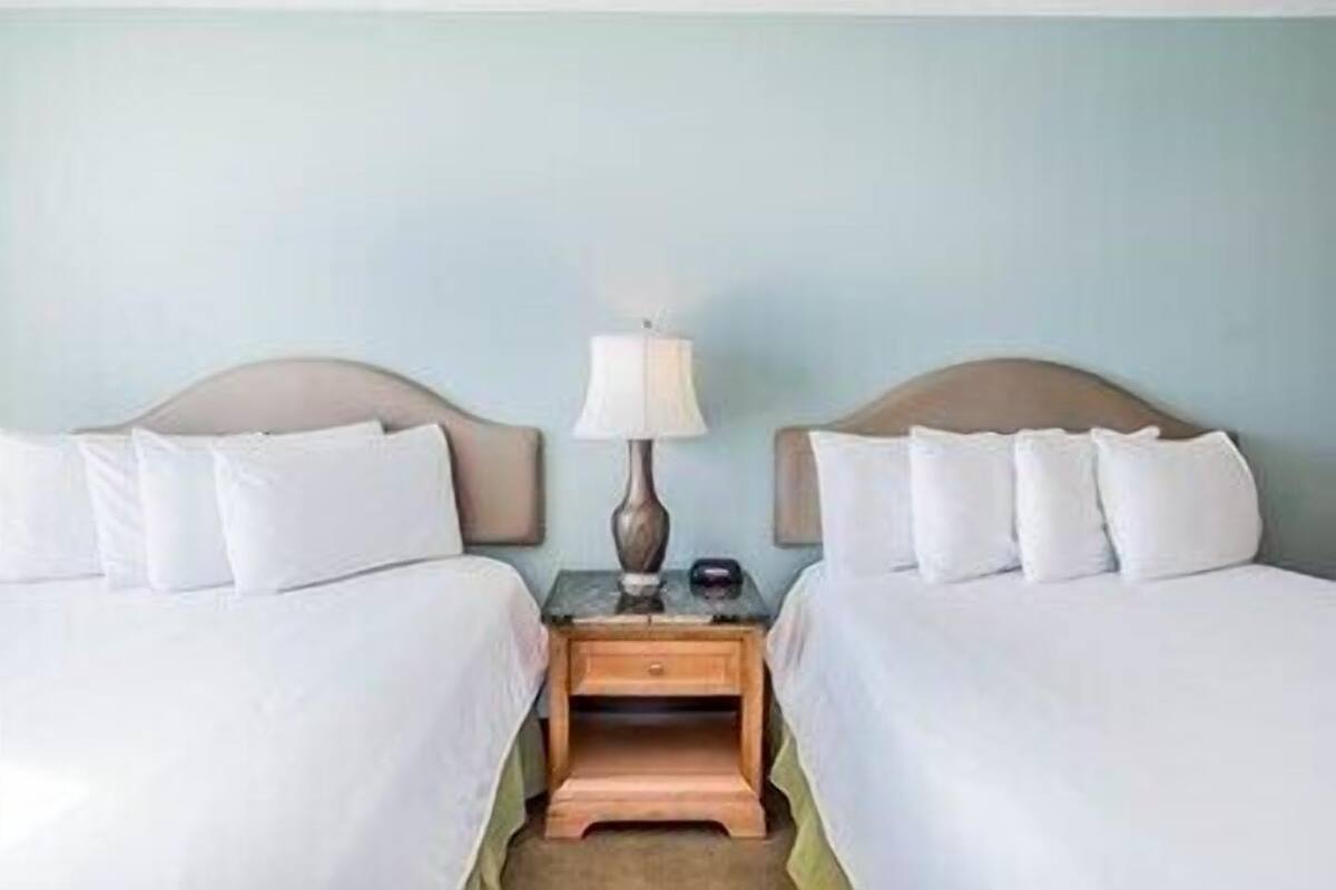 A hotel room with two beds, a nightstand with a lamp, and a small wooden stool.