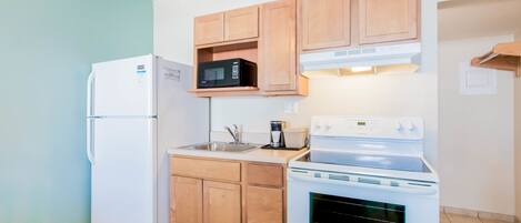 Une cuisine de taille réduite équipée d’un réfrigérateur, d’un four à micro-ondes, d’une cuisinière et de meubles de rangement en bois.