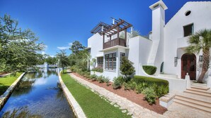 A modern white building with a pool, a wooden pergola, and a staircase leading to the entrance.