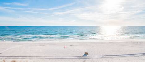 A beach with a wooden walkway leading to the water, a lifeguard tower, and a clear sky.