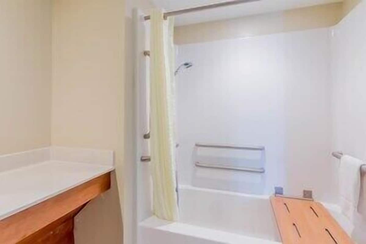 A bathroom with a shower, a wooden bench, and a towel rack.