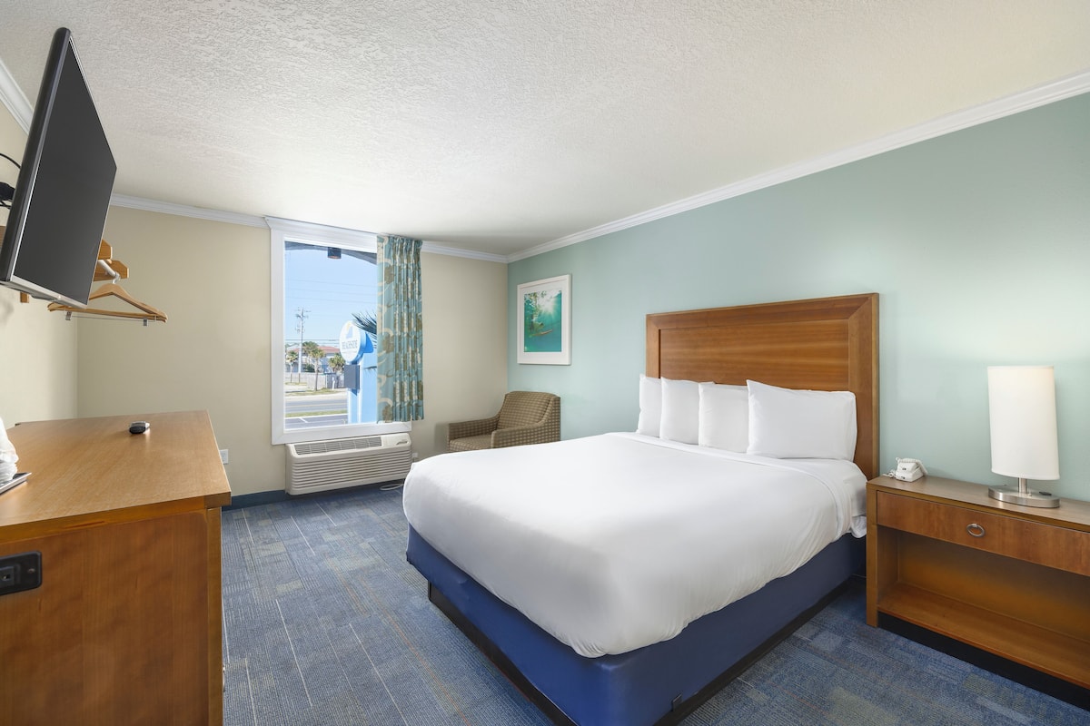 A hotel room with a large bed, a desk, a chair, a TV, and a window with curtains.
