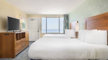 Habitación de hotel con dos camas, televisor, cómoda de madera, ventana con vista al mar y una puerta.
