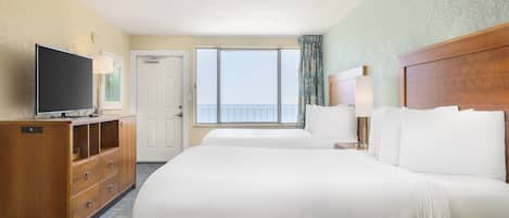 Habitación de hotel con dos camas, televisor, cómoda de madera, ventana con vista al mar y una puerta.