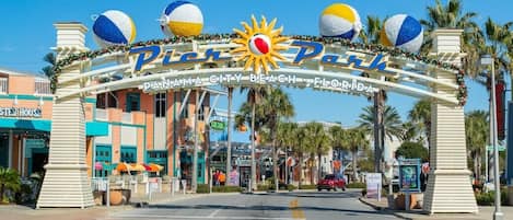 The entrance to Pier 70, featuring a sun and beach ball decoration, palm trees, and a clear blue sky.