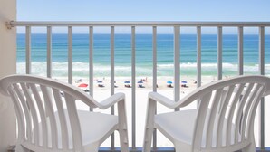 A balcony with white chairs overlooking a beach with umbrellas and people.