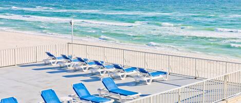 Un balcon donnant sur la plage, avec des chaises longues bleues et une rambarde d’où l’on peut admirer l’océan.