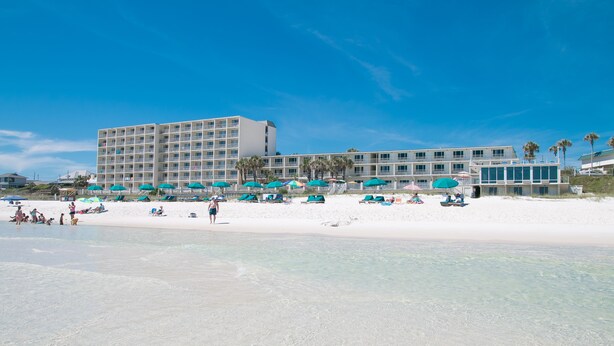 A beachfront hotel with multiple balconies, beach umbrellas, and a sandy beach.