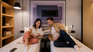 Una habitación moderna con dos camas, una estantería, una obra de arte enmarcada y una lámpara.