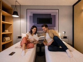 A modern room with two beds, a bookshelf, a framed artwork, and a lamp.