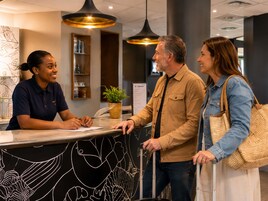 A reception desk with a black and white abstract design, a potted plant, and a menu board in a modern lobby with pendant lighting.