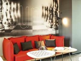 A modern hotel lobby with a red sofa, a small round table, and a wall with a neon sign.