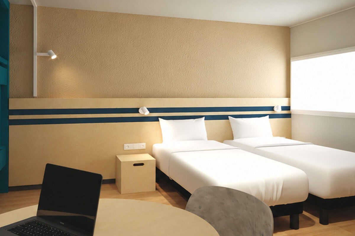 A hotel room with a bed, bedside tables, a desk with a laptop, and a window.