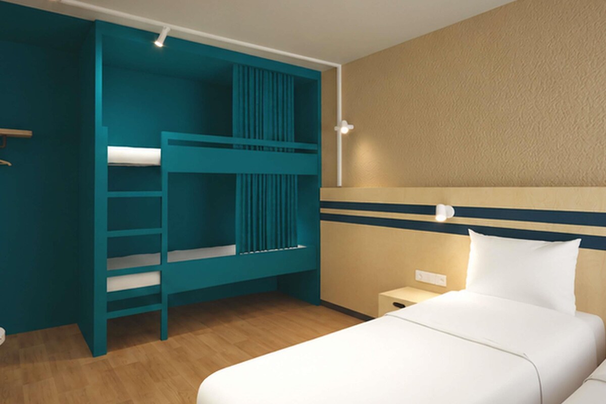 Habitación de hotel con literas, una mesita de noche y un aplique de pared.
