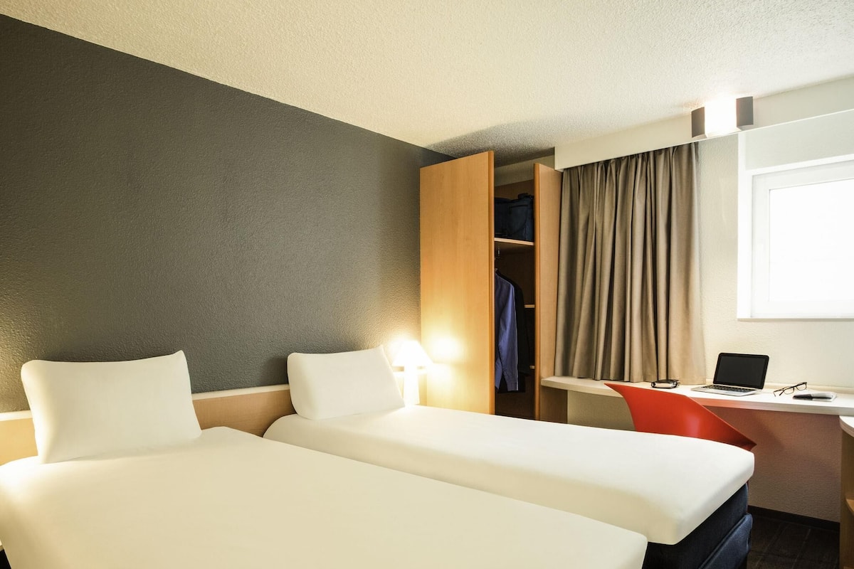 Habitación de hotel con dos camas, un escritorio con una computadora portátil, una silla y un armario.