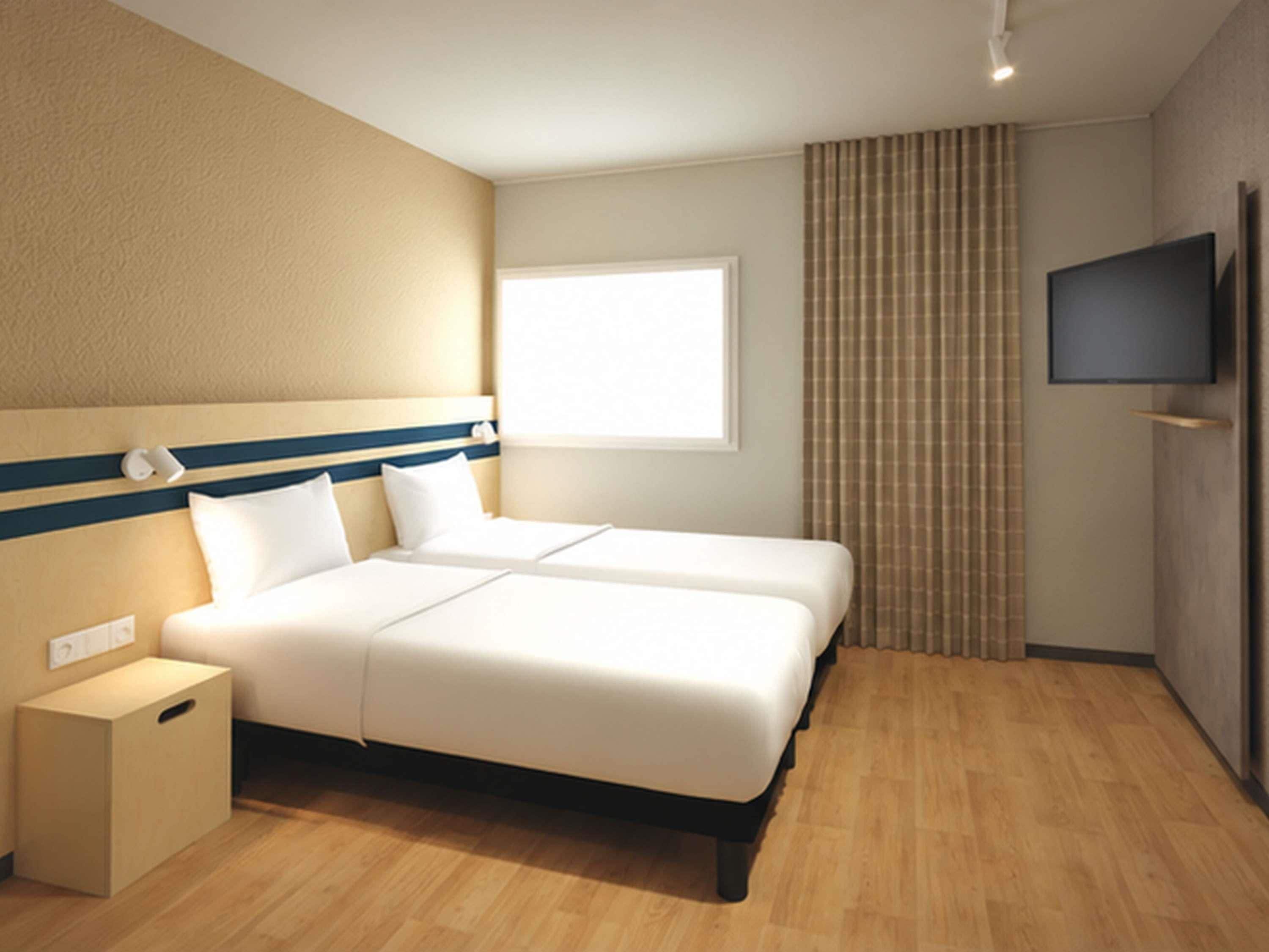 A hotel room with a bed, bedside tables, a TV, and a window.