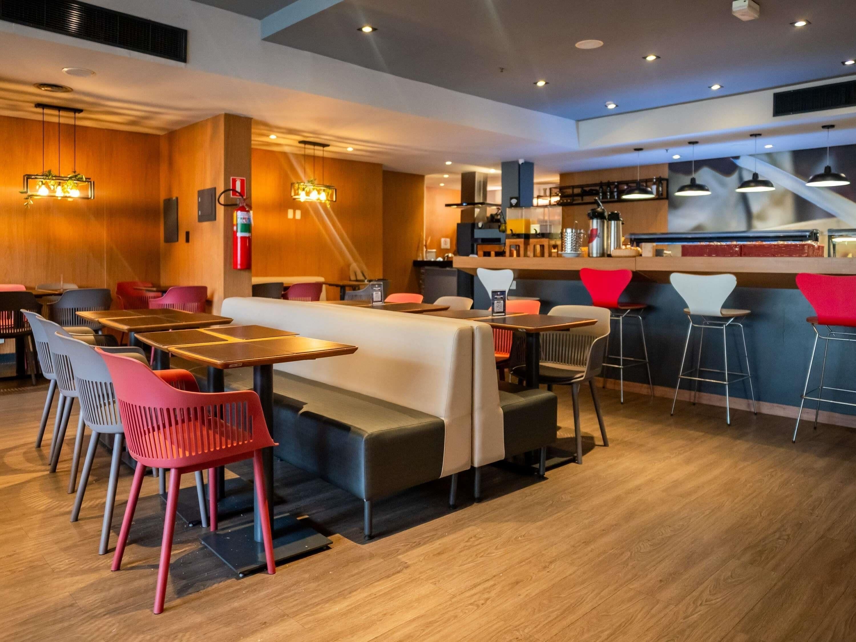 Ein modernes Restaurant mit Holzboden, mehreren Sitzbereichen, darunter Boxsitzgelegenheiten und Barhocker, sowie Pendelleuchten.