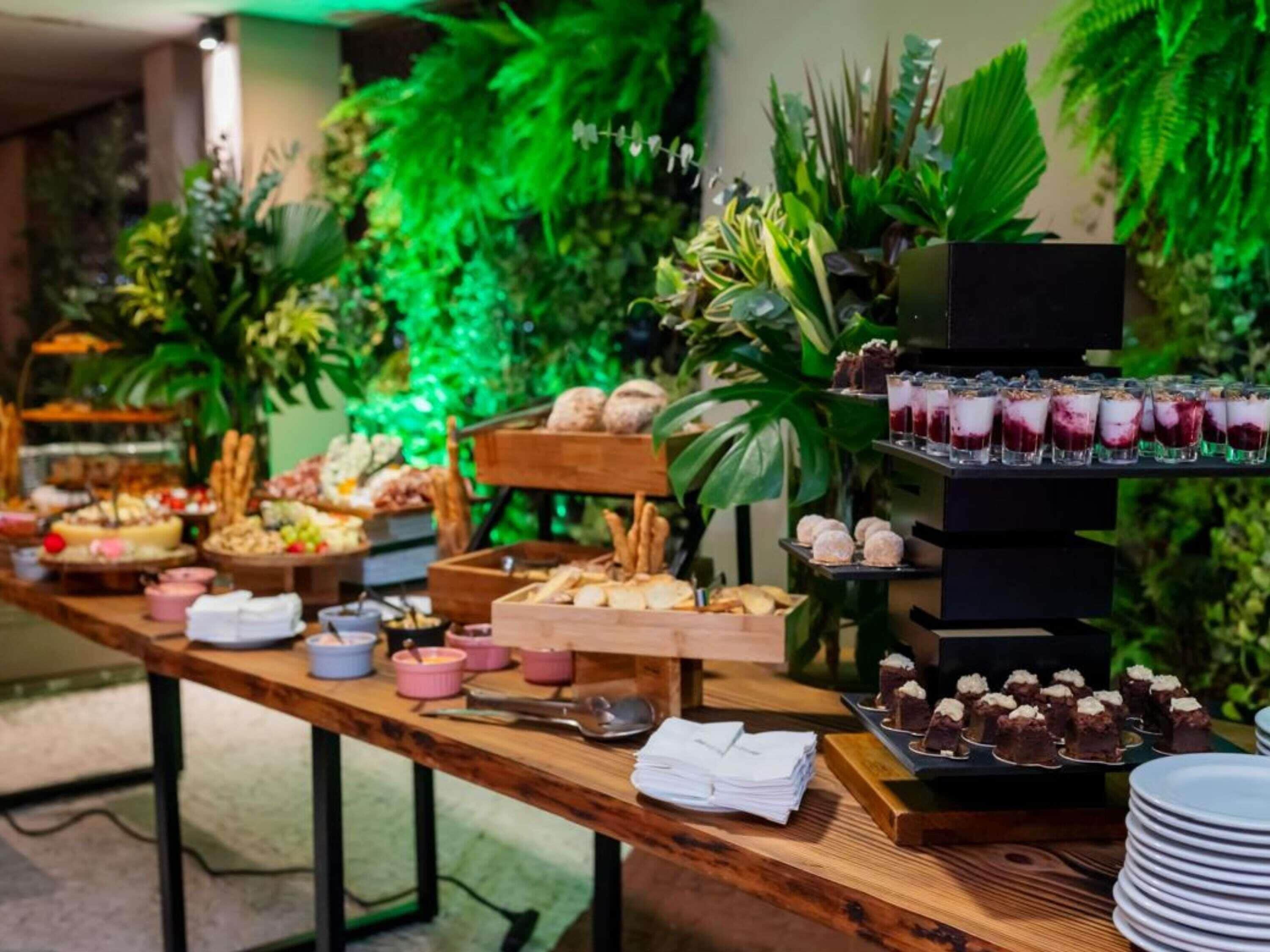 Mesa de buffet com diversos pratos e um canto de sobremesas.