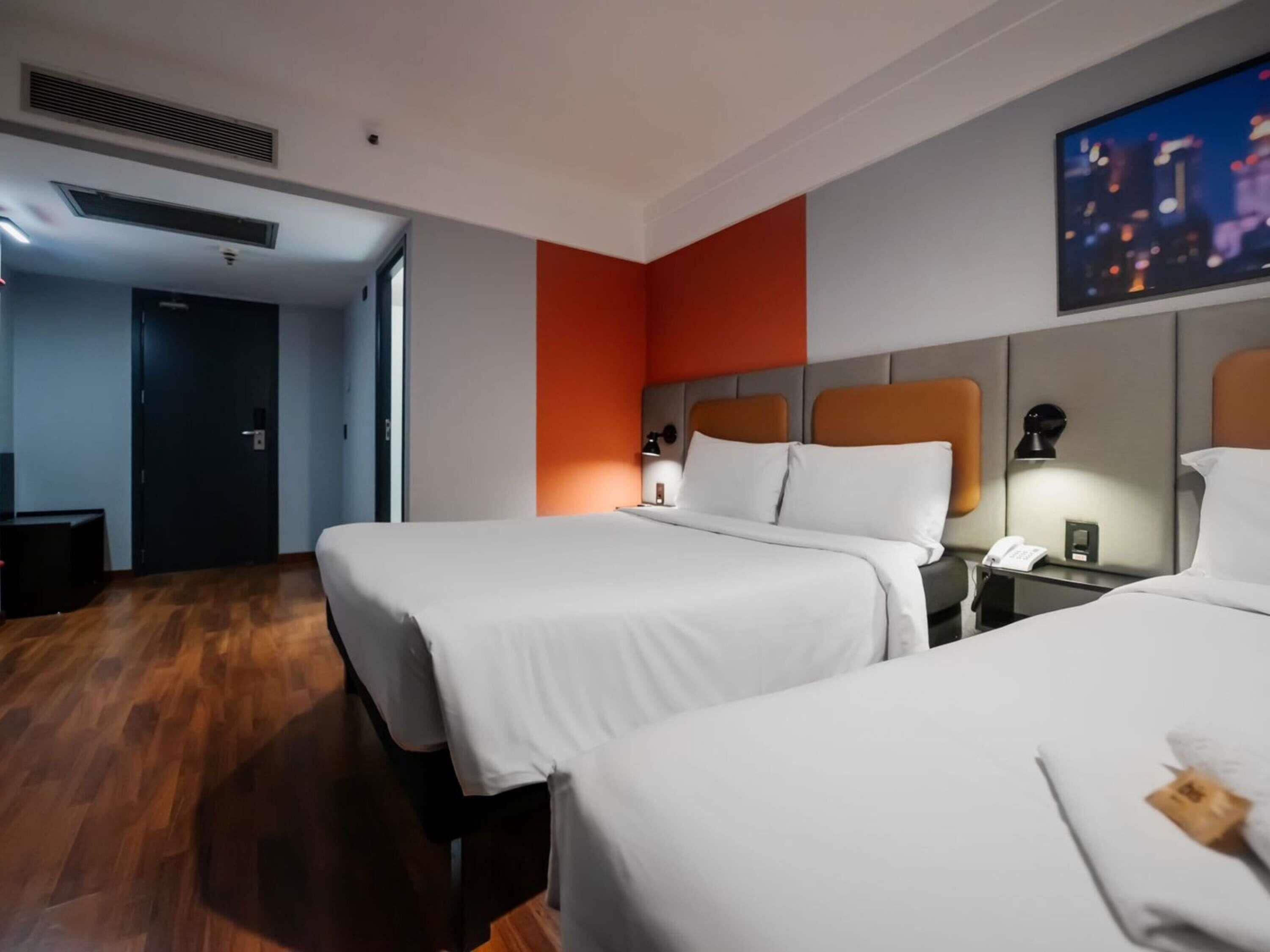 A hotel room with two beds, a flat-screen TV, a desk with a lamp, and a painting on the wall.