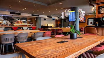 A modern restaurant with wooden tables and chairs, a bar area, and a digital menu display.